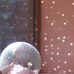 Boule à facettes miroir sur rebord de fenêtre avec reflets lumineux sur mur rose.