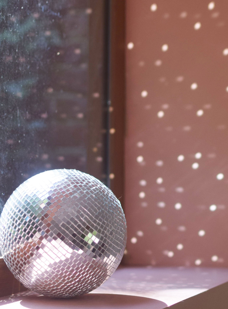 Boule à facettes miroir sur rebord de fenêtre avec reflets lumineux sur mur rose.