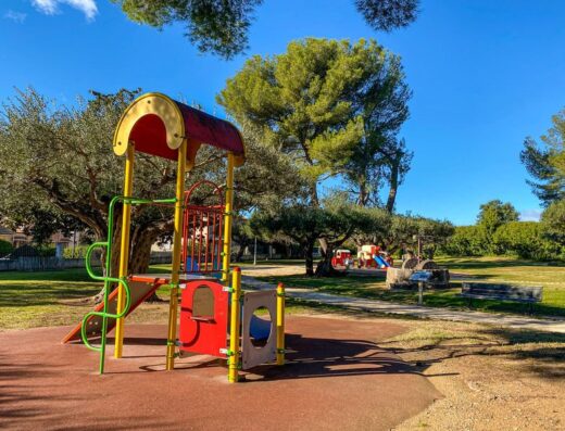 Aire de jeux colorée pour enfants avec toboggan dans un parc arboré sous un ciel bleu.