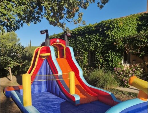 Château gonflable avec toboggan aquatique et piscine pour enfants dans un jardin ensoleillé.