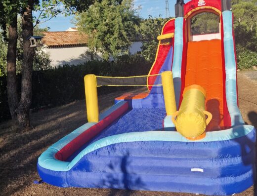 Château gonflable pirate avec toboggan aquatique et piscine pour enfants dans un jardin.
