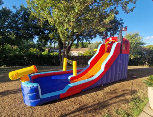 Toboggan gonflable pirate avec piscine pour enfant dans un jardin ensoleillé.