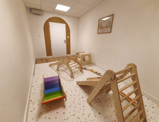 Aire de motricité libre Crea-Kid avec triangle de Pikler, arche en bois et parcours d'éveil pour enfants dans une salle de jeux moderne.