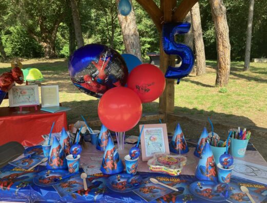 Décoration d'anniversaire Spiderman pour enfant de 5 ans en extérieur avec ballons, assiettes et chapeaux de fête thématiques.