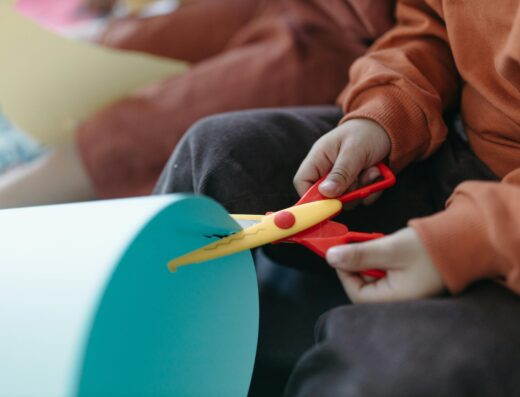 Enfant découpant du papier cartonné bleu avec des ciseaux cranteurs en plastique lors d'une activité créative