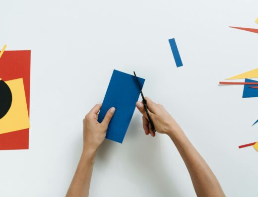 Mains découpant un rectangle de papier bleu avec des ciseaux sur un plan de travail créatif blanc.